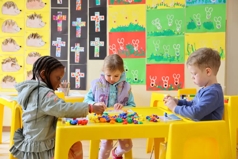 Children working together at a yellow table beneath their cross artworks