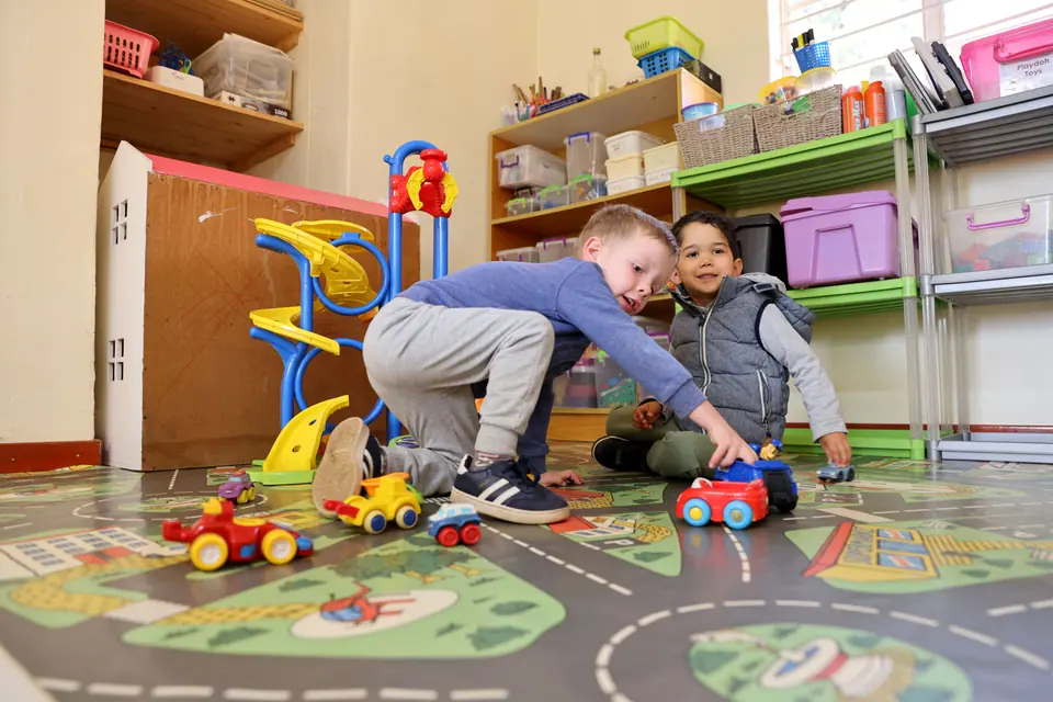 Two boys playing with toy cars on a road-map play mat