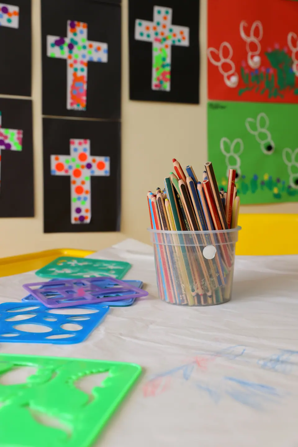 Stencils and coloured pencils on a table beneath children’s cross artworks