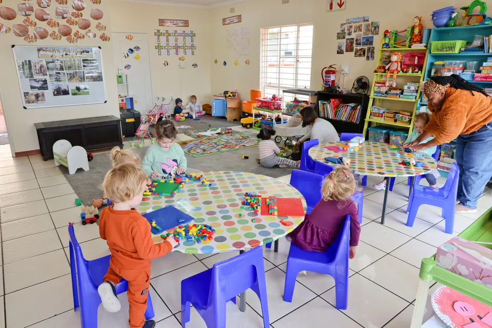 Children playing at small tables in a sunny classroom