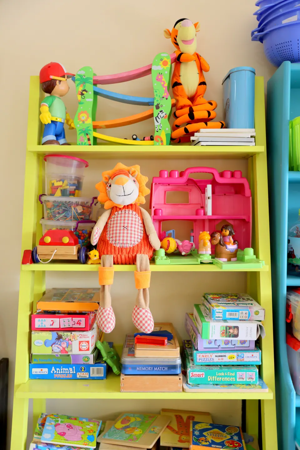 A bright green toy shelf with puzzles, dolls and soft toys