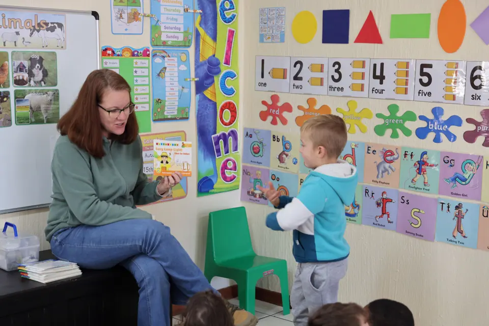 A teacher and a young boy pointing out numbers and shapes on a classroom wall display