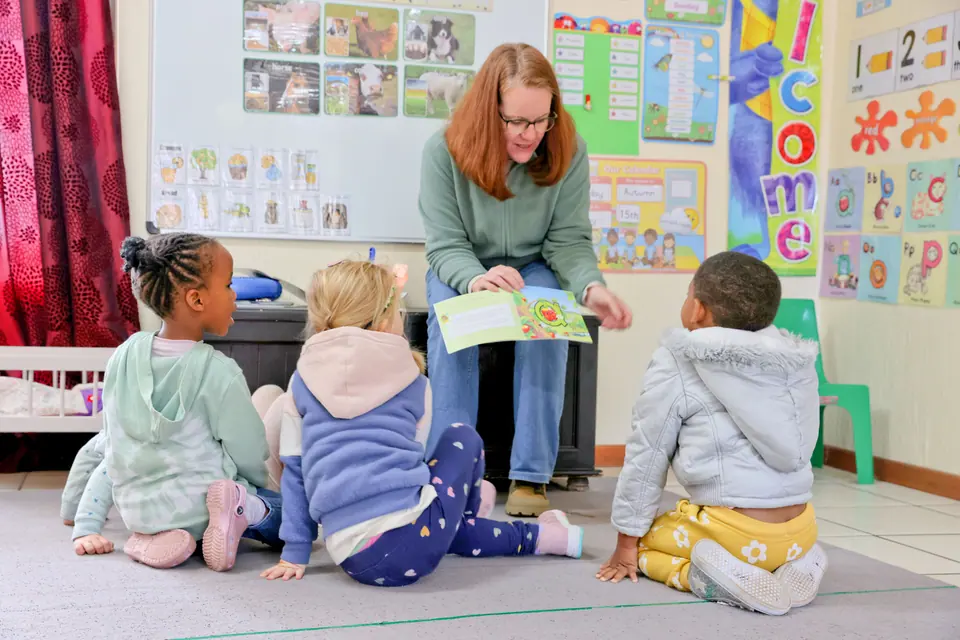 A teacher reading a story to children seated on the floor