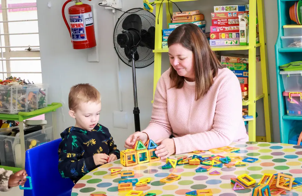 A teacher building with colourful magnetic tiles alongside a young boy