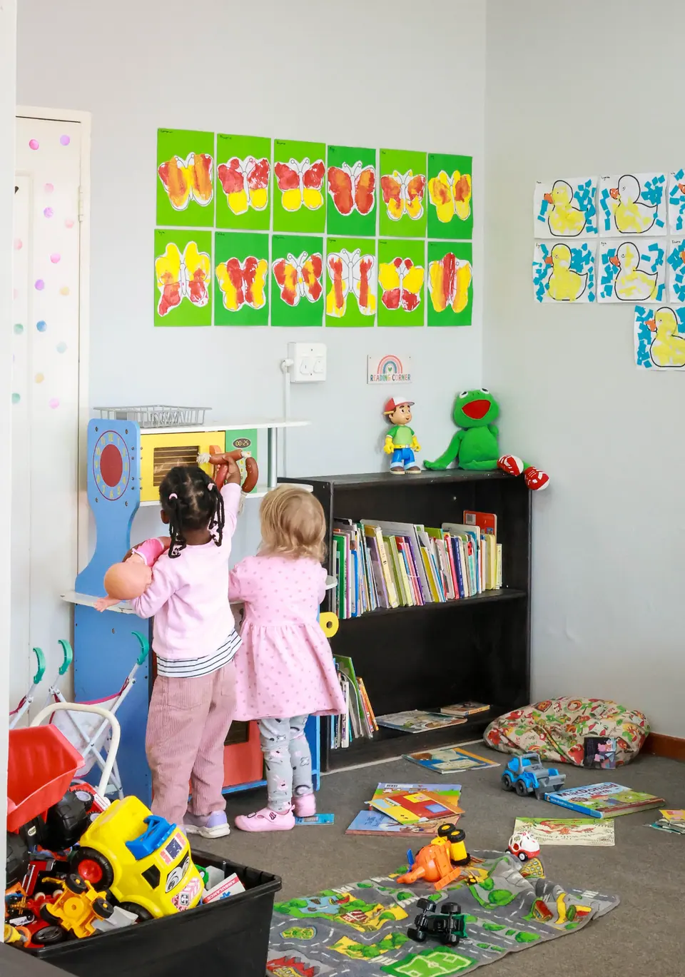 Two little girls playing with a toy kitchen in a bright playroom