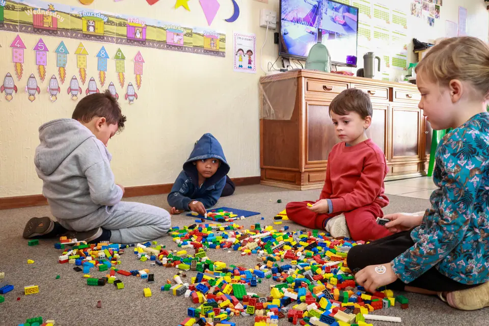 Children building together on a carpet covered in colourful bricks