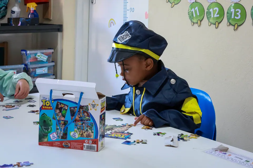 A boy in a dress-up police hat concentrating on a jigsaw puzzle