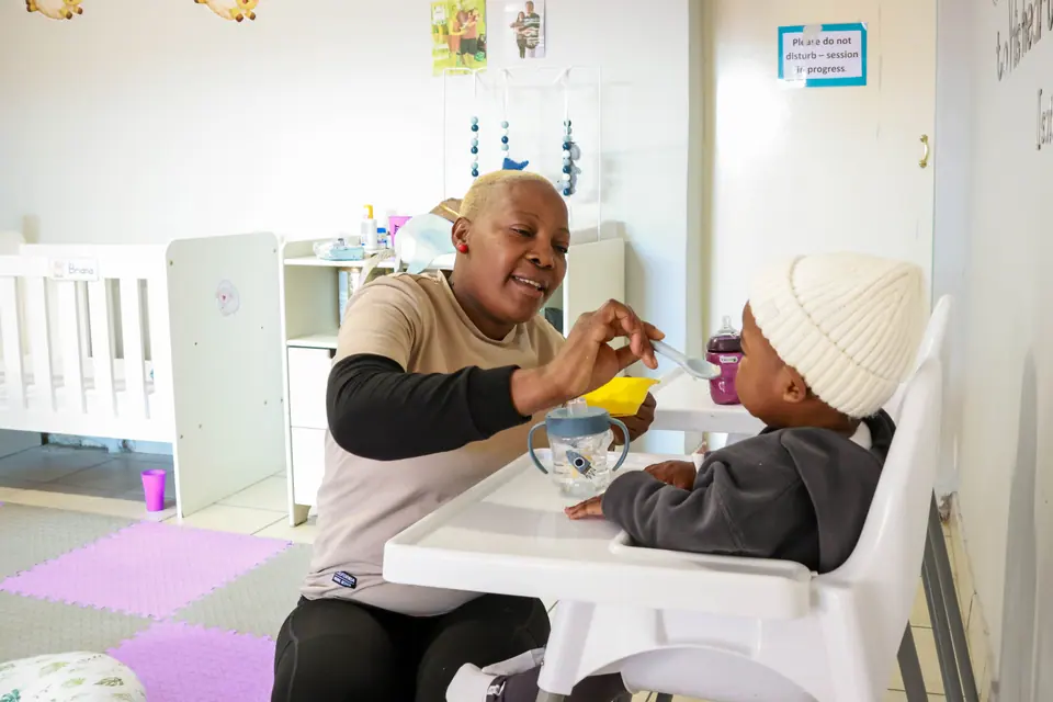 A caregiver feeding a baby in a high chair