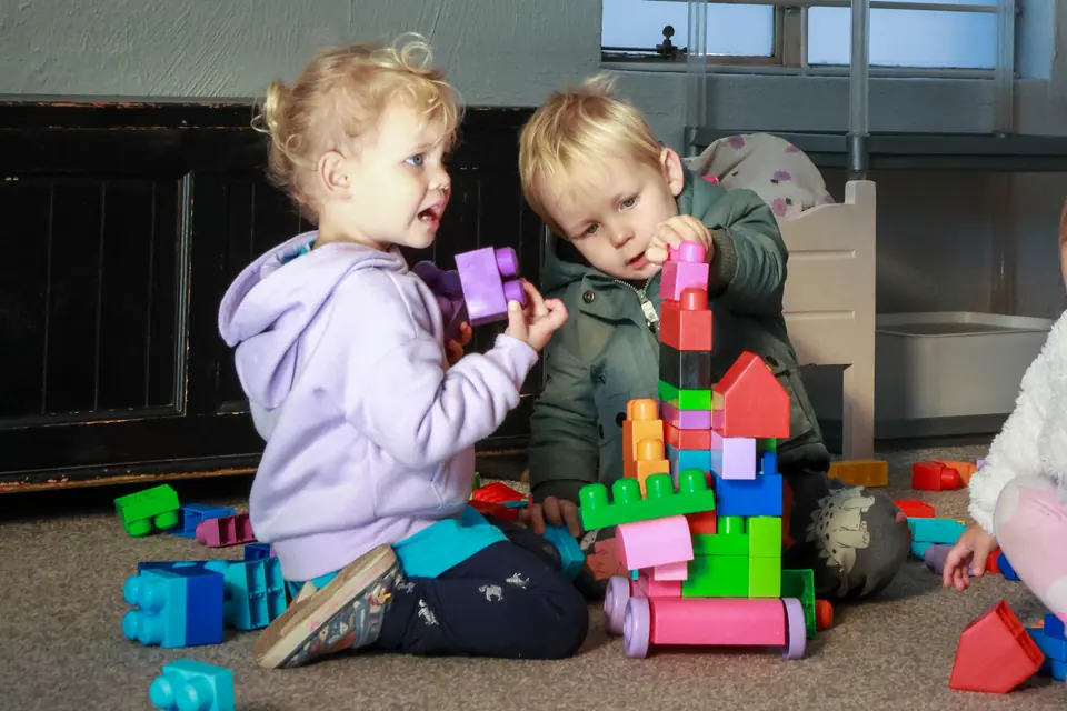 Two toddlers building a tower together with large blocks