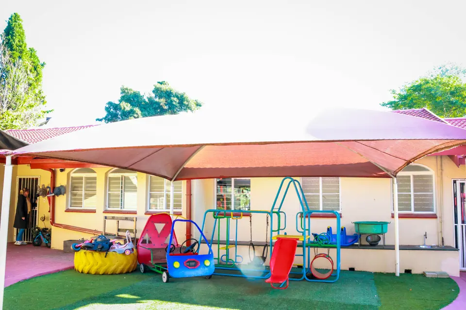 The shaded outdoor play area with ride-on toys and climbing frames