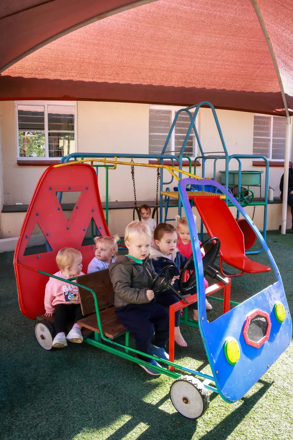Toddlers sitting together in a red and blue play car