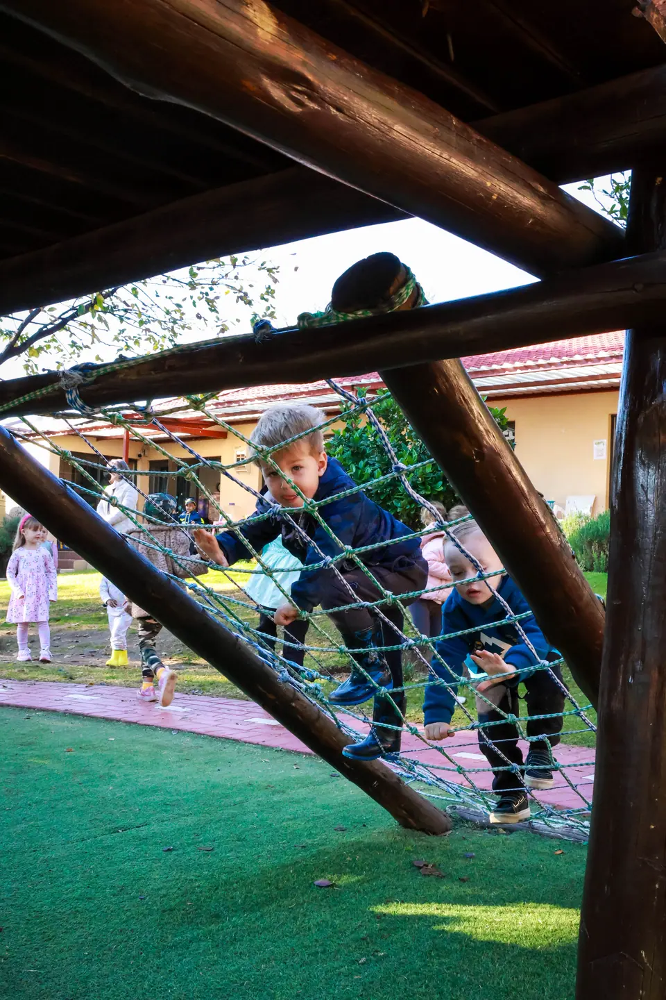 Children climbing a rope net beneath the wooden jungle gym
