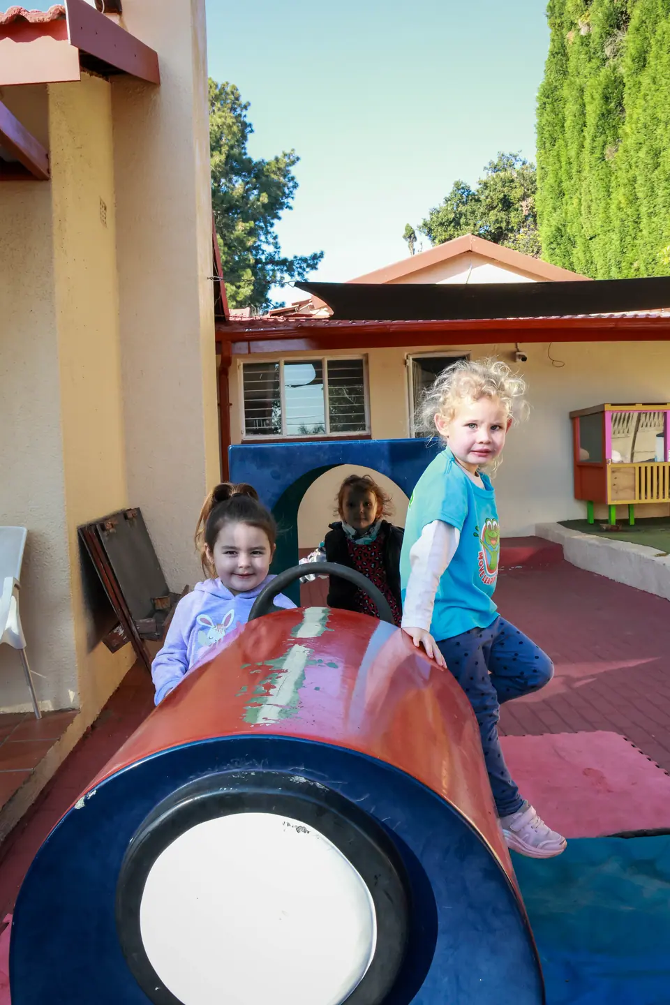 Two smiling girls playing on a play tunnel in the courtyard