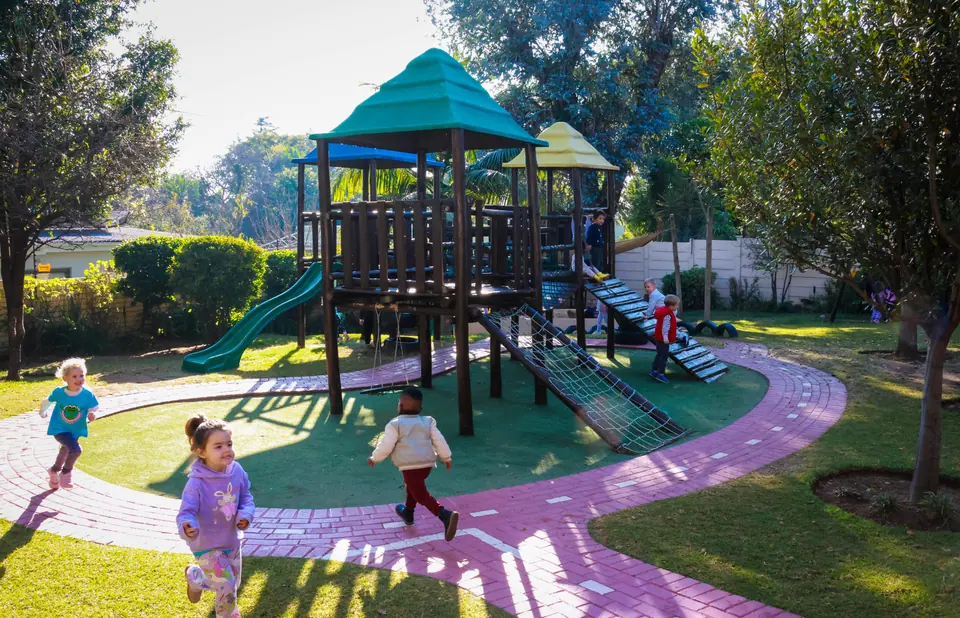 Children running along the garden path towards the wooden jungle gym