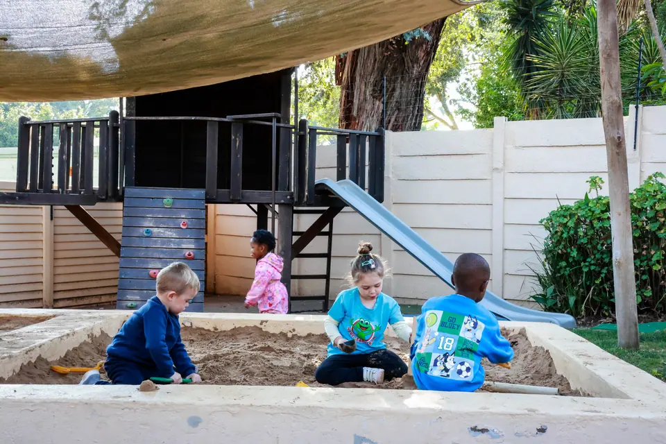 Children digging in the sandpit beside a wooden playhouse