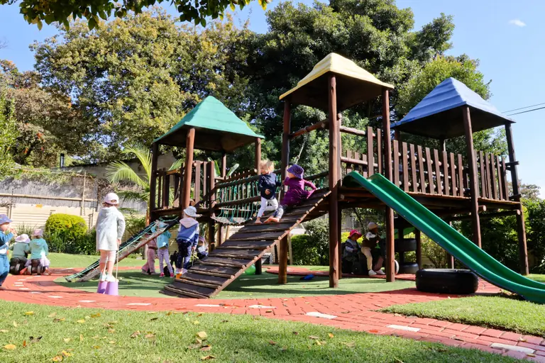 Children playing on the wooden jungle gym and green slide on a sunny day