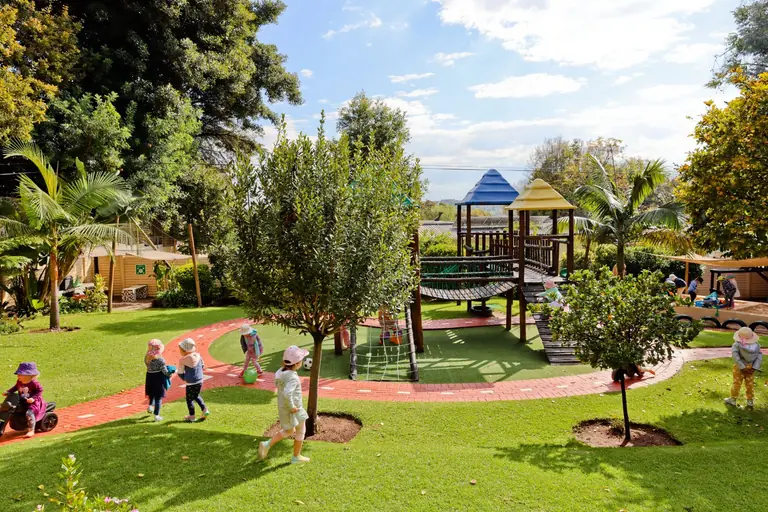 Children playing in the school garden, with palm trees, a winding path and the wooden jungle gym